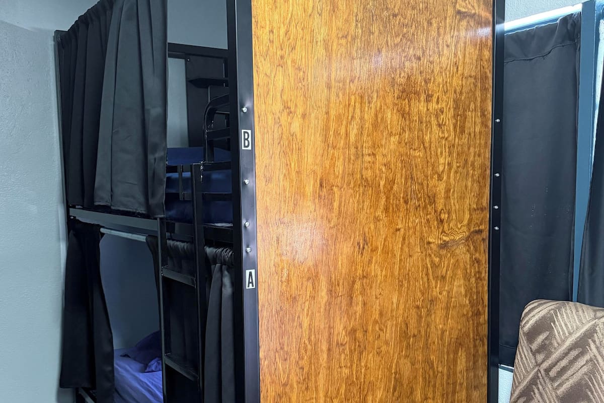 Een stapelbed met een houten paneel, een stoel en een wandplank met opbergdozen.