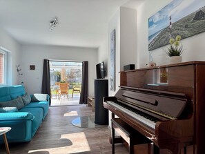 Ein Wohnzimmer mit einem Klavier, einem türkisfarbenen Sofa und einem Essbereich mit Stühlen und einem Tisch.