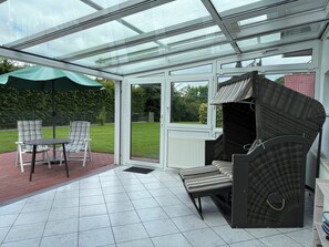 A conservatory with a glass roof, a patio area with a table and chairs, and a seating area with a wicker sofa.