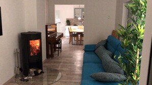 A living room with a wood-burning stove, a piano, a dining area, and a blue sofa. - Apartment Wilhelmine ground floor - winter garden, quiet and central in Aurich Ostfriesland (Aurich)
