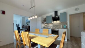A modern kitchen with a dining area, wooden chairs, a piano, and a hanging light fixture. - Apartment Wilhelmine ground floor - winter garden, quiet and central in Aurich Ostfriesland (Aurich)