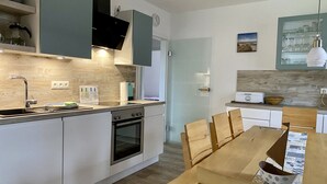 A modern kitchen with a built-in oven, a sink, and a dining area with a wooden table and chairs. - Apartment Wilhelmine ground floor - winter garden, quiet and central in Aurich Ostfriesland (Aurich)