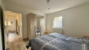A bedroom with a bed, a wardrobe, a mirror, a window, and a radiator. - Apartment Wilhelmine ground floor - winter garden, quiet and central in Aurich Ostfriesland (Aurich)