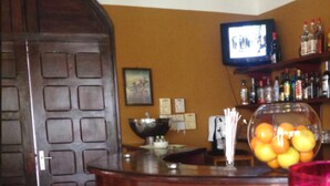 A bar area with a wooden counter, red bar stools, a television mounted on the wall, and a bowl of fruit on the counter. - Archotel (Dakar)