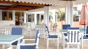 An outdoor patio area with white and blue chairs and tables, surrounded by potted plants and umbrellas. - Archotel (Dakar)