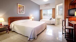 A hotel room with a large bed, a smaller bed, a desk with a chair, a television, and a window with curtains. - Archotel (Dakar)