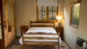 A bedroom with a wooden bed, a nightstand, a lamp, and a window with a view of trees. - La Floridita Puerto Piramides (Puerto Pirámides)