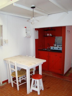 Ett litet kök med ett rött skåp, ett vitt bord och en pall.