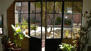 A room with a large window divided into multiple panes, potted plants inside, and a view of an outdoor area with trees and a building in the background. - La Floridita Puerto Piramides (Puerto Pirámides)