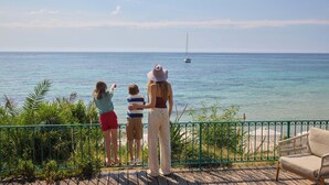 A balcony with a view of the sea, a sailboat, and a chair. - Forte Village Resort Villa Del Parco & Spa (Pula)