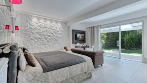 A modern bedroom with a large bed, a sofa, a TV, and a stone wall. - Forte Village Resort Villa Del Parco & Spa (Pula)