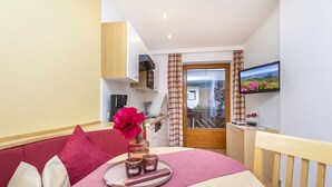 A hotel room with a bed, a dining table with a tray of food, a TV on the wall, and a view of the outside. - Ferienhaus Eva (Flachau)