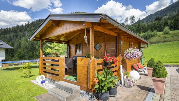 A wooden cabin with a porch, outdoor seating, and potted plants. - Ferienhaus Eva (Flachau)