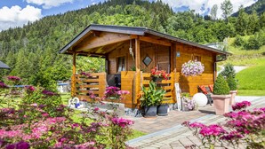 A wooden cabin with a porch, surrounded by lush greenery and flowers. - Ferienhaus Eva (Flachau)