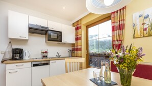A modern kitchen with white cabinets, a microwave, a coffee maker, and a dining area with a table, chairs, and a vase of flowers. - Ferienhaus Eva (Flachau)