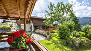 A wooden balcony with a potted red flower arrangement, a stone wall, and a view of a mountain landscape. - Ferienhaus Eva (Flachau)