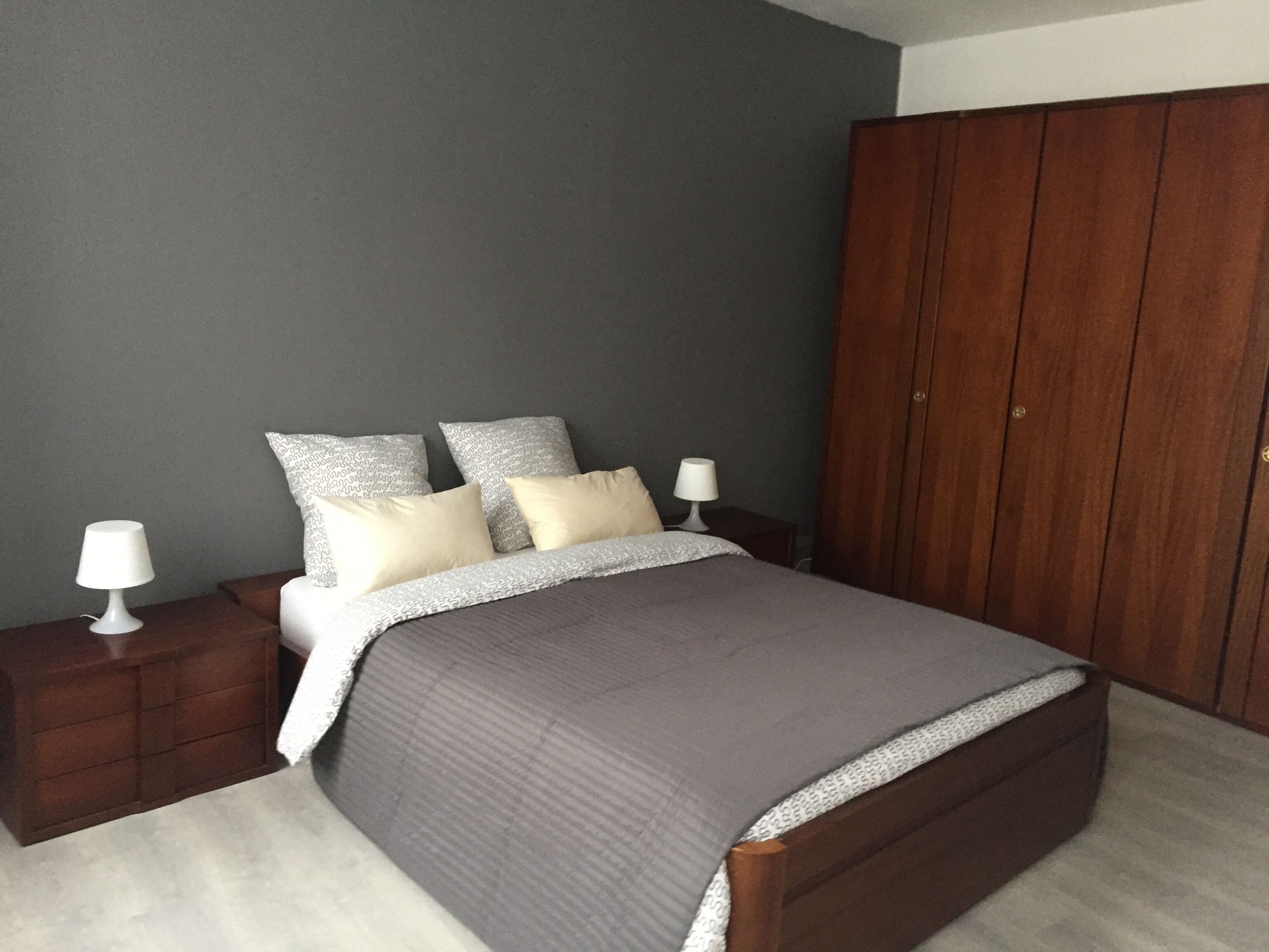 A bedroom with a bed, two bedside tables, a wardrobe, and a grey wall.