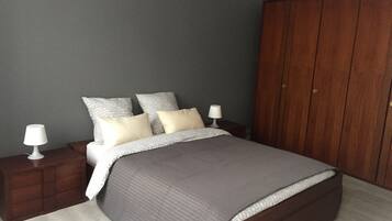A bedroom with a bed, two bedside tables, a wardrobe, and a grey wall.