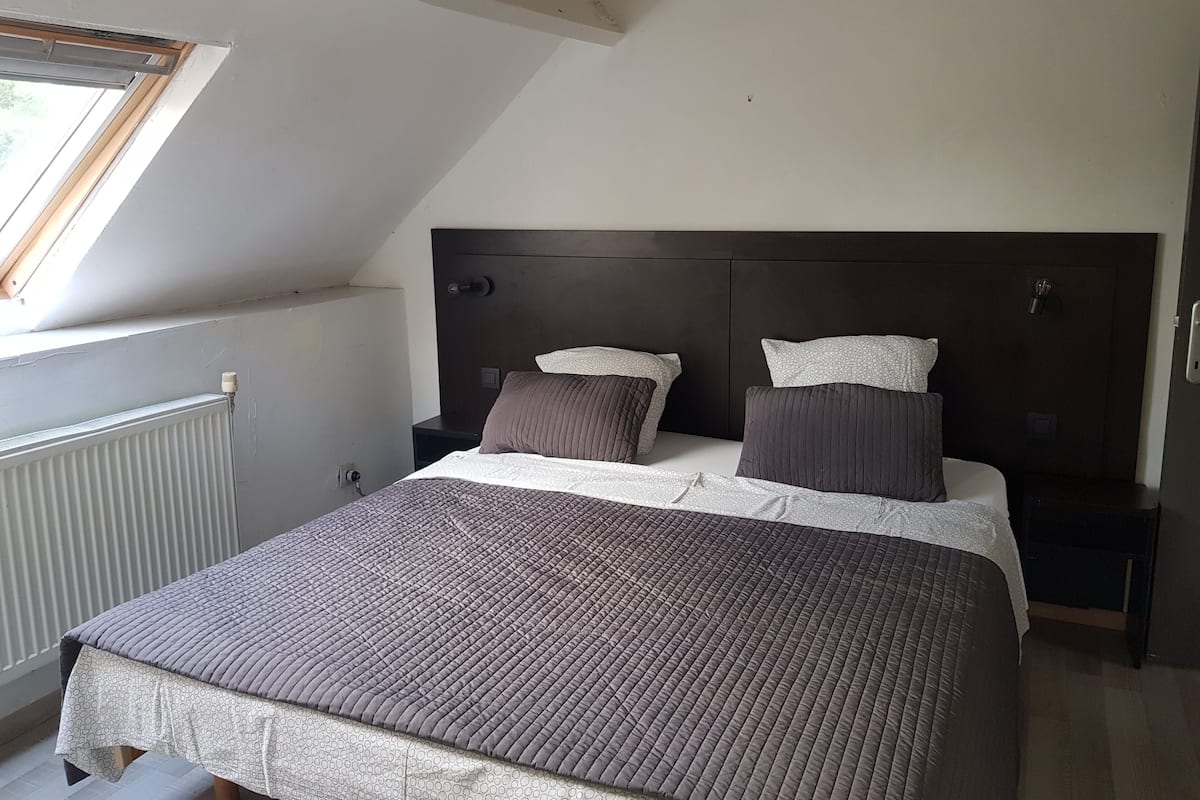 A bedroom with a sloped ceiling, a bed with a dark headboard, two bedside tables, and a window with a view of the outdoors.