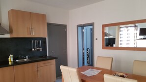 A modern kitchen with wooden cabinets, a black countertop, and stainless steel appliances. There is a dining area with a wooden table and beige chairs. - Appartements bon Secours (Peruwelz)