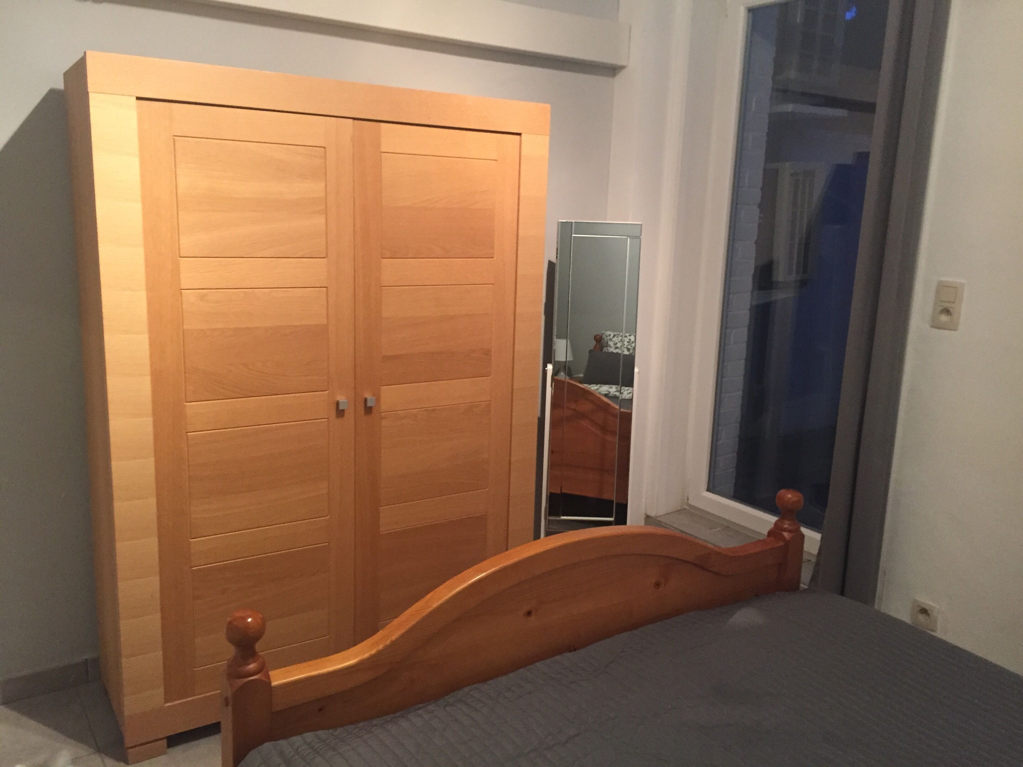 Un dormitorio con un armario de madera, una cama con cabecera de madera y un ventanal con vistas al exterior.