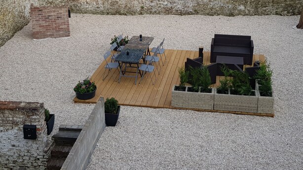 A patio area with a wooden deck, a table with chairs, and potted plants. - Appartements bon Secours (Peruwelz)