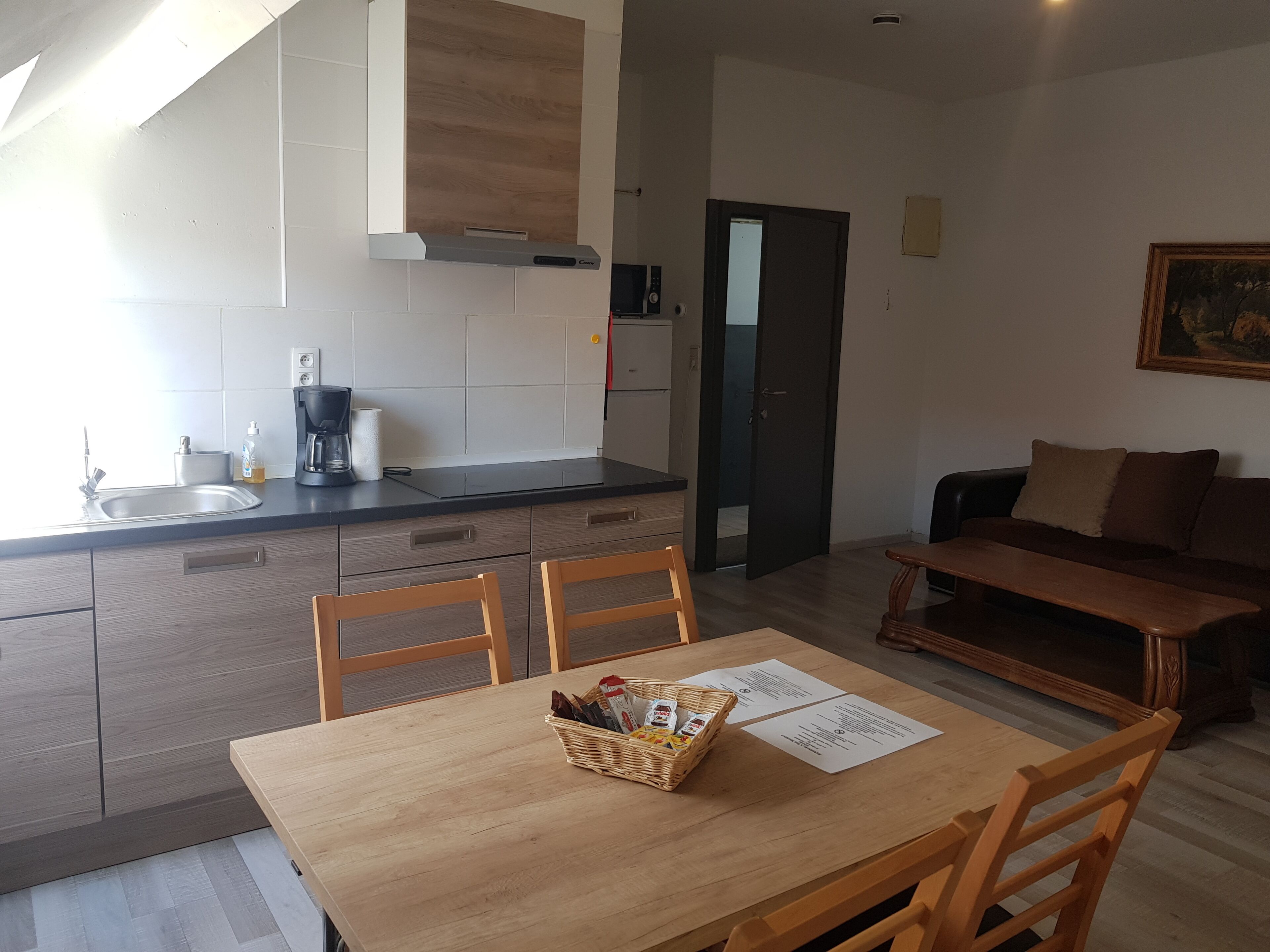 Une cuisine moderne avec une table et des chaises en bois, une machine à café et un panier rempli de collations.