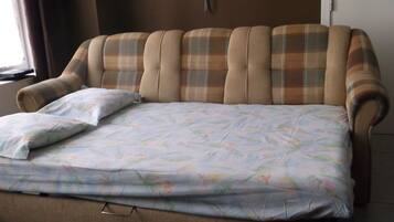 A bed with a floral bedspread and a pillow, a headboard with a plaid pattern, and a wall-mounted light fixture.