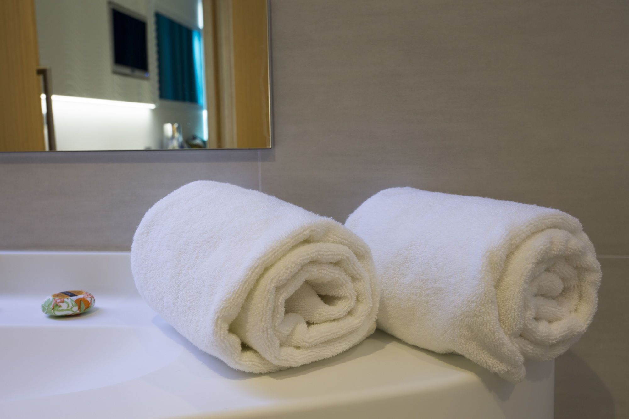 Two rolled white towels on a white bathroom sink.