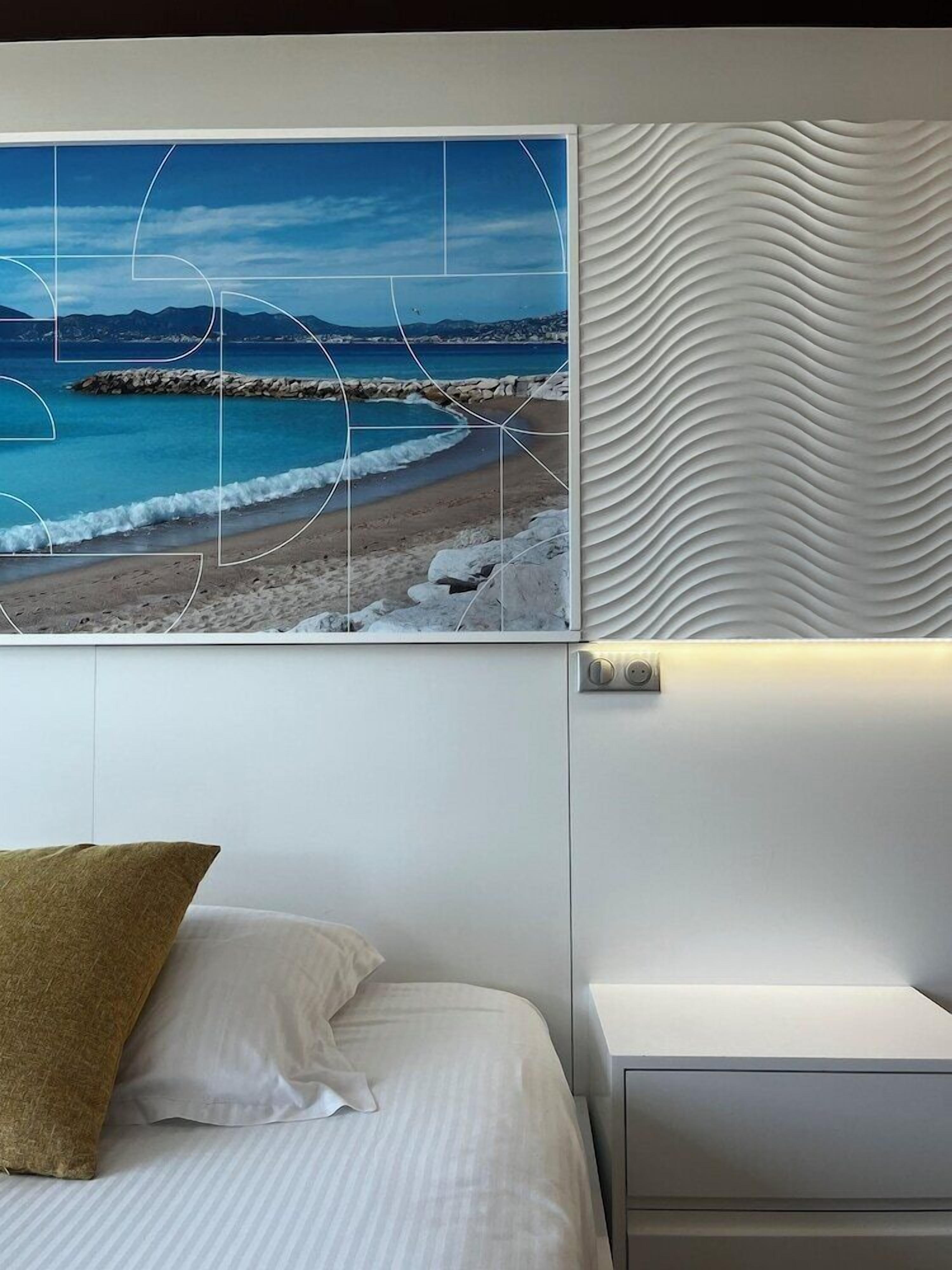 A bedroom with a bed, a nightstand, and a wall-mounted picture of a beach scene.