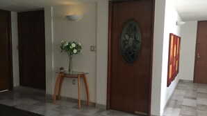 A hallway with a glass-top table, a vase with flowers, a decorative door, and a tiled floor. - Departamento en Centro de Toluca (Toluca)
