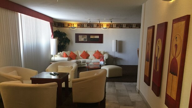 A modern living room with a sofa, armchairs, a coffee table, and a dining table. There are framed artworks on the wall and a plant in the corner. - Departamento en Centro de Toluca (Toluca)