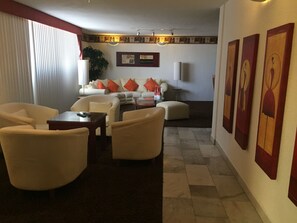 A modern living room with a sofa, armchairs, a coffee table, and a dining table. There are framed artworks on the wall and a plant in the corner.