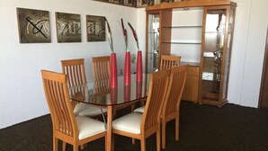A dining area with a glass table surrounded by wooden chairs, three red vases, and wall art. - Departamento en Centro de Toluca (Toluca)