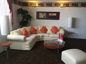 A living room with a beige sectional sofa, orange pillows, a glass coffee table, and a large potted plant. - Departamento en Centro de Toluca (Toluca)