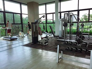 Un gimnasio con máquinas de cardio, equipo de levantamiento de pesas y amplias ventanas que ofrecen vistas a zonas verdes.