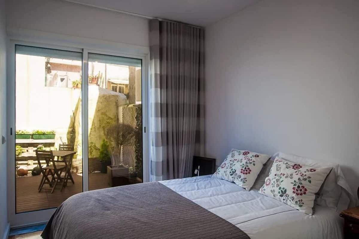 A bedroom with a bed, a sliding glass door leading to an outdoor area, and a curtain on the window.