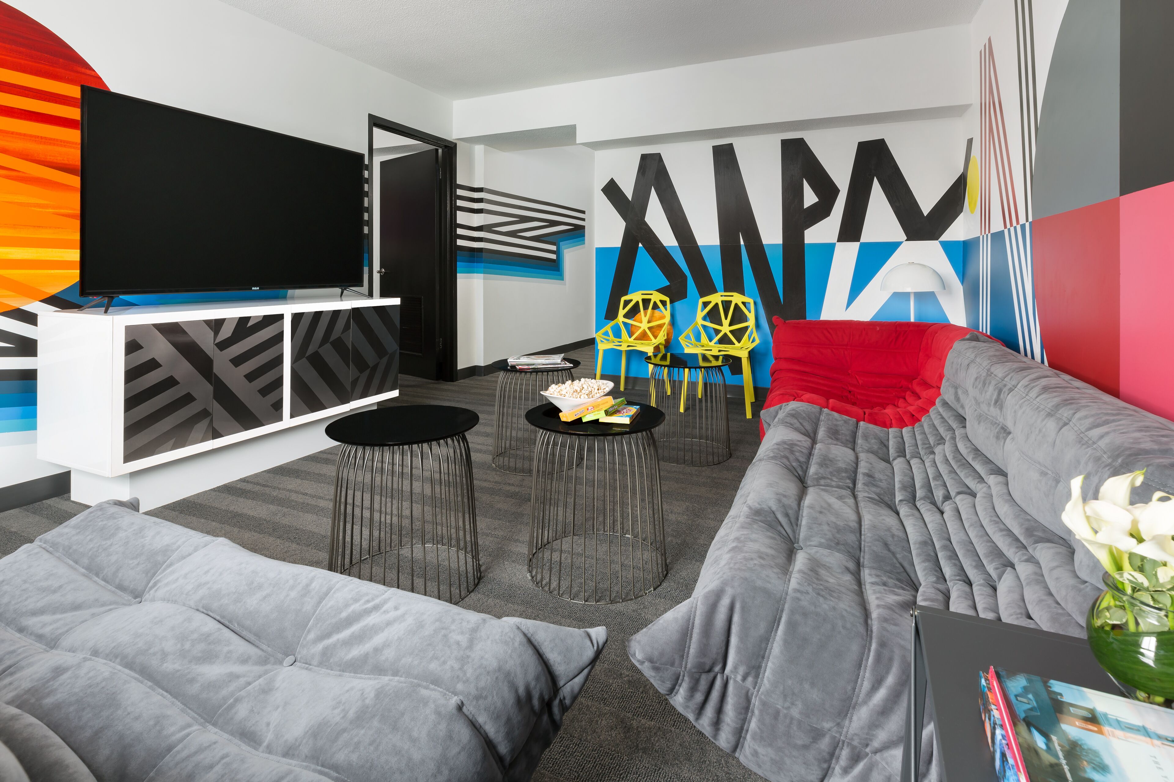A modern living room with a grey sofa, a flat-screen TV, and a vibrant abstract mural.