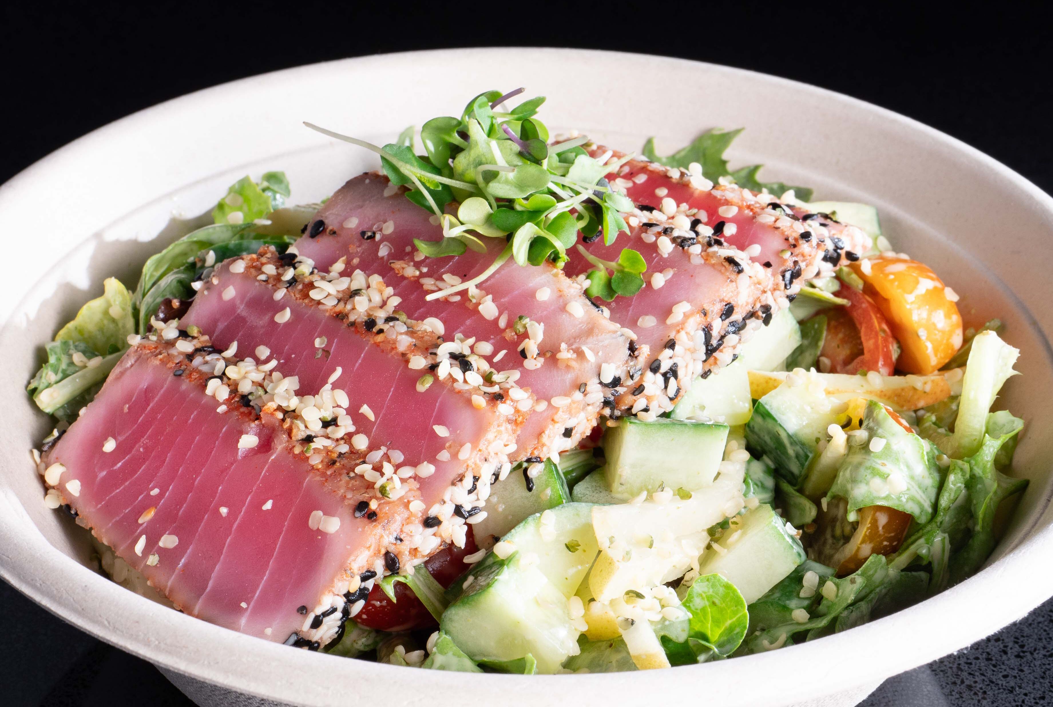 A bowl of sashimi with sesame seeds and greens.