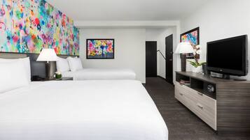 Habitación de hotel con dos camas, televisión, escritorio con lámpara y obras de arte en las paredes.
