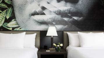 Habitación de hotel con dos camas, una mesita de noche con lámpara, un florero con flores y un cuadro abstracto grande en la pared.