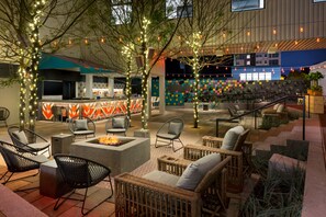 An outdoor seating area with wicker furniture, a fire pit, and string lights.
