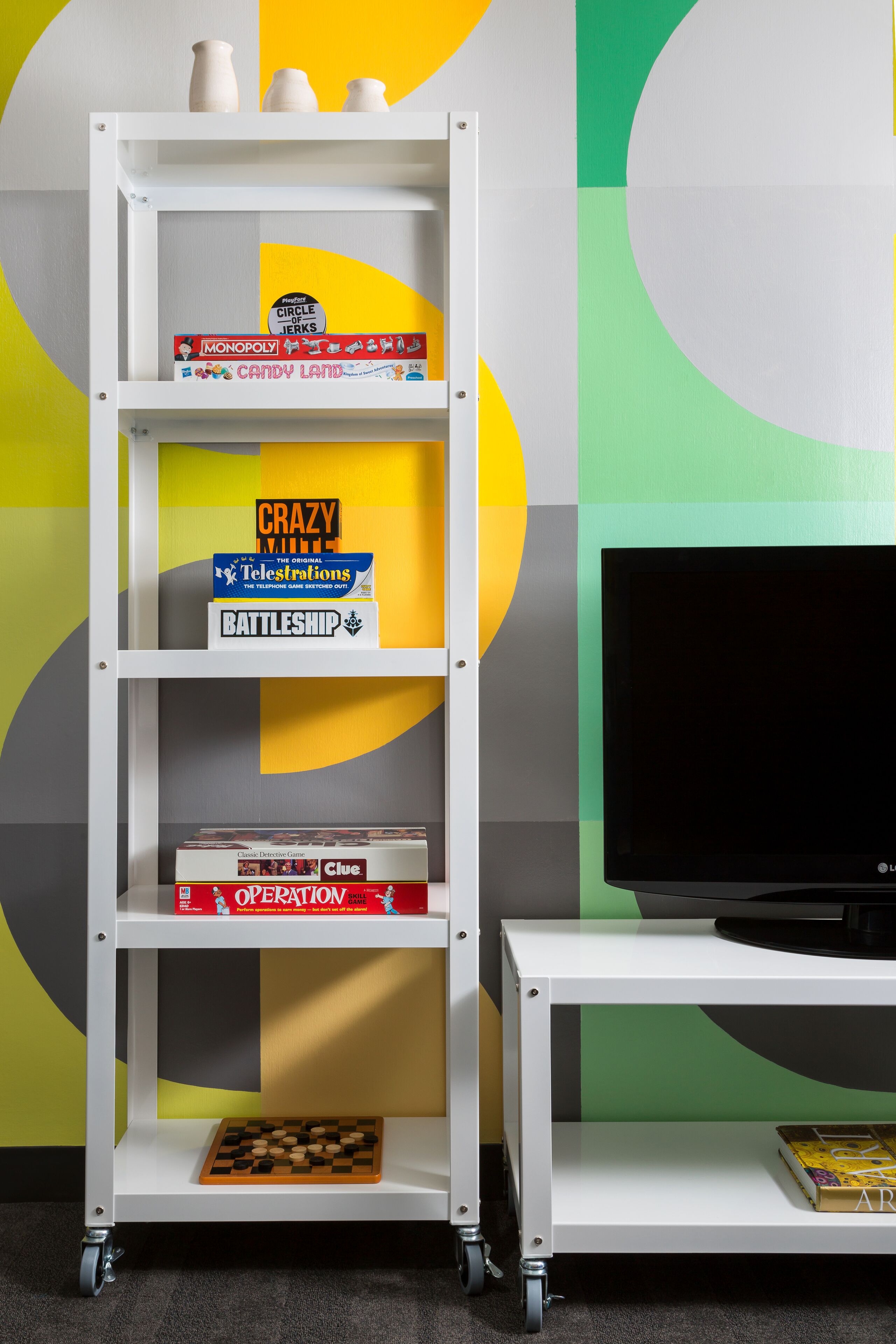 Una estantería blanca con varios juegos de mesa y un televisor sobre un soporte.