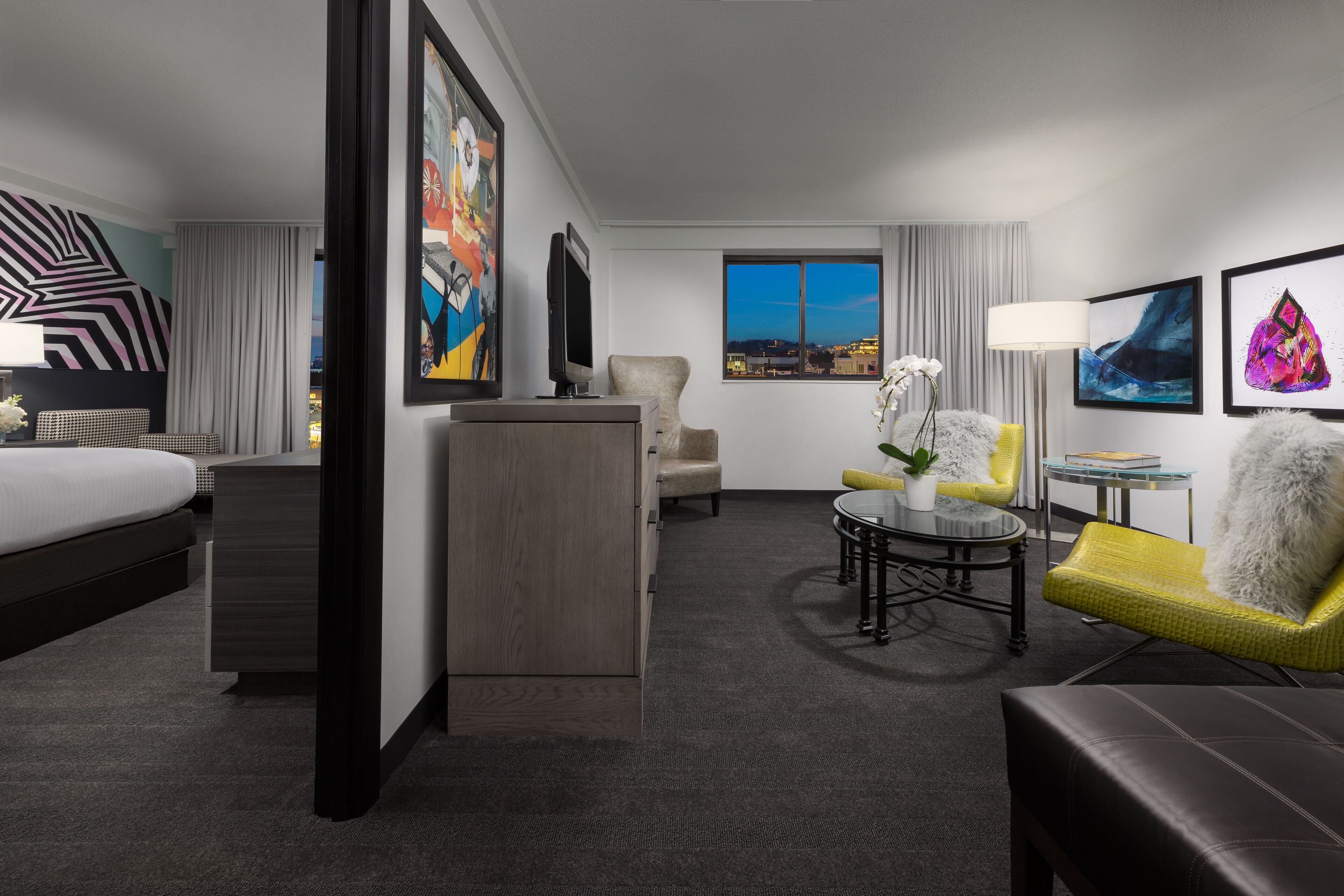 Una habitación de hotel con cama, escritorio, sillón, sofá y obras de arte en las paredes.