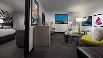 Una habitación de hotel con cama, escritorio, sillón, sofá y obras de arte en las paredes.