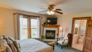 A bedroom with a bed, a fireplace, a chair, and a door leading to a bathroom. - Country Hermitage B&B (Williamsburg)