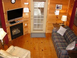 A cozy cabin interior with a television, fireplace, plaid sofa, and wooden walls.