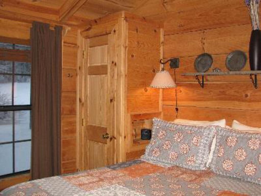 Un dormitorio de cabaña de madera con una cama, una lámpara colgante y un estante con platos decorativos.