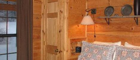 Un dormitorio de cabaña de madera con una cama, una lámpara colgante y un estante con platos decorativos.