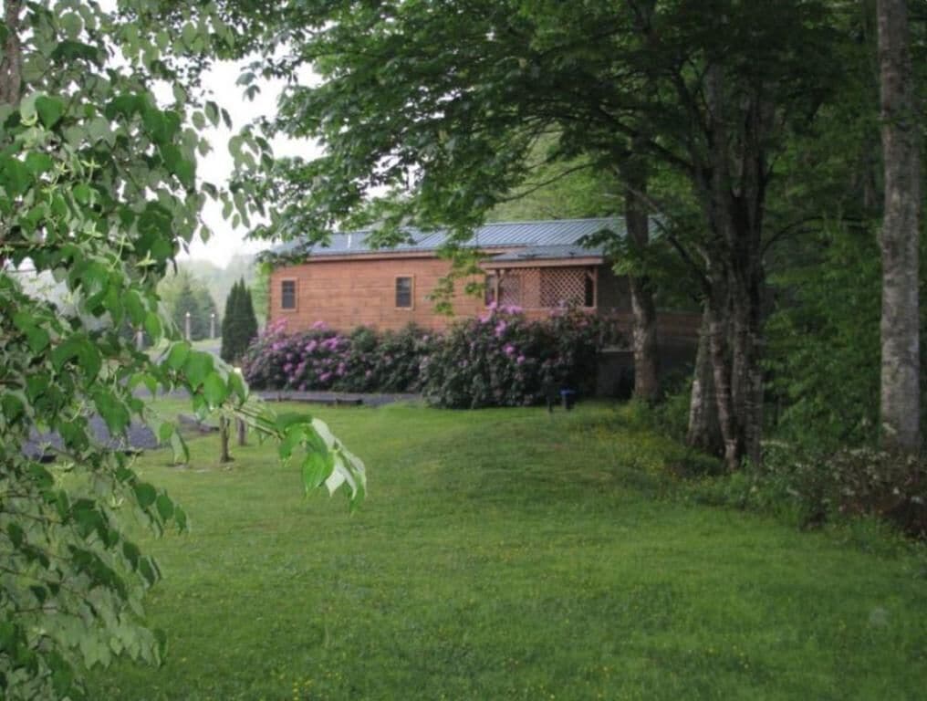 Uma casa de tijolos com telhado inclinado, cercada por um gramado e árvores.